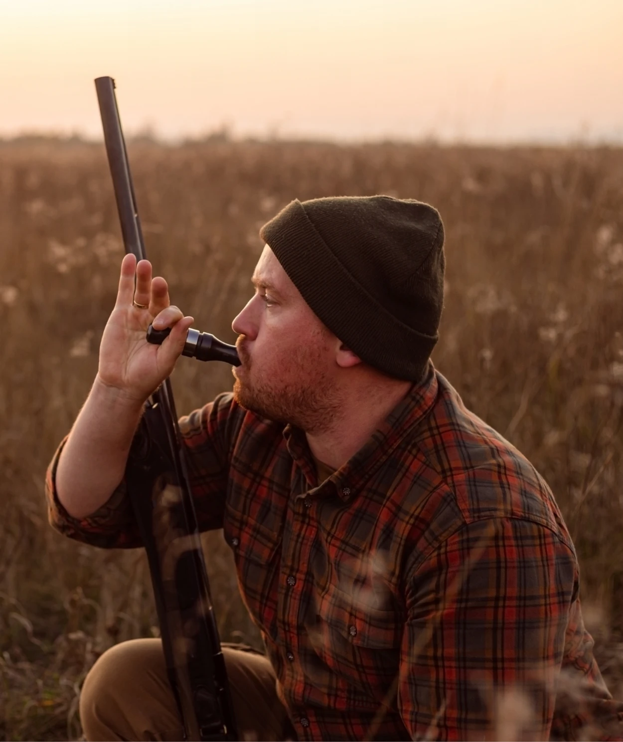 Hunter using a duck call in field.